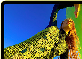 MacBook Neo, citrus colour, screen shows a smiling person lying in a sunny field of flowers