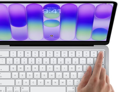 MacBook Neo, silver colour, showing login screen, person’s finger on Touch ID sensor in top-right corner of keyboard