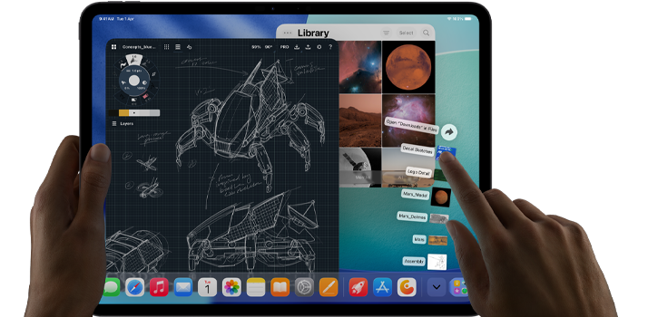 iPad Pro, space black colour, left hand holding device, right hand pointing gesturing to manipulate multiple open app windows, a drawing app with sketches of mechanical designs, photos library of planets and space images, downloads folder files fanned out