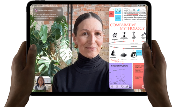 iPad Pro, front exterior, landscape orientation, space black colour, rounded corners, black display bezel, hands holding left and right sides, display showing a FaceTime conversation being live translated, and an educational app showing a presentation of “Comparative Mythology” with text, diagrams and handwritten notes