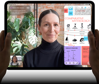 iPad Pro, front exterior, landscape orientation, space black colour, rounded corners, black display bezel, hands holding left and right sides, display showing a FaceTime conversation being live translated, and an educational app showing a presentation of “Comparative Mythology” with text, diagrams and handwritten notes