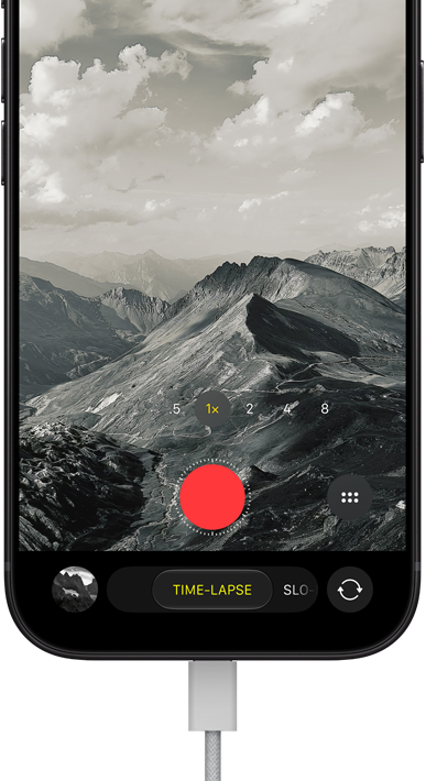 iPhone 18 Pro, front exterior, displaying a mountainous landscape, with the camera mode overlay in Time-Lapse mode, with power cord attached to charging port
