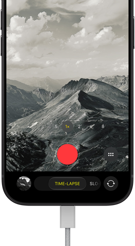 iPhone 18 Pro, front exterior, displaying a mountainous landscape, with the camera mode overlay in Time-Lapse mode, with power cord attached to charging port