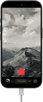 iPhone 18 Pro, front exterior, displaying a mountainous landscape, with the camera mode overlay in Time-Lapse mode, with power cord attached to charging port