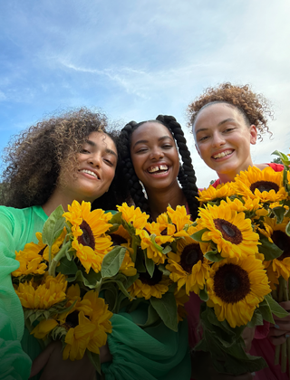 A sharp and vibrant selfie of three people holding flowers.