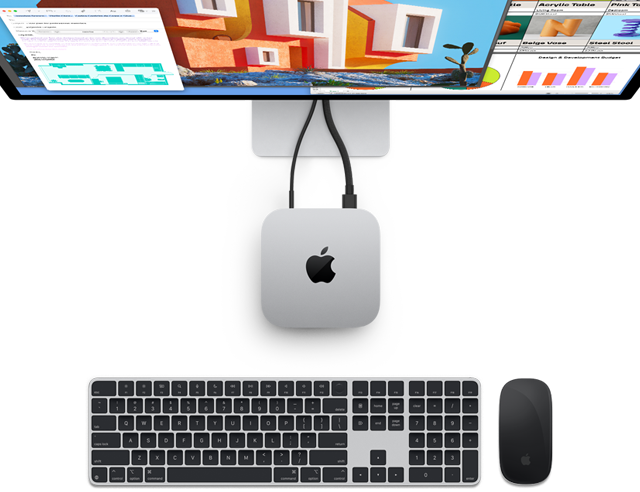 Top of silver Mac mini with Apple logo, shown plugged into a monitor and next to a wireless Magic Keyboard and Magic Mouse