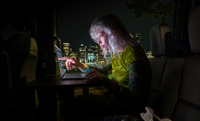 A person in a mobile studio, visible through the open van door, working on a MacBook Pro with PROLED XDR Display, at a remote location near mountains